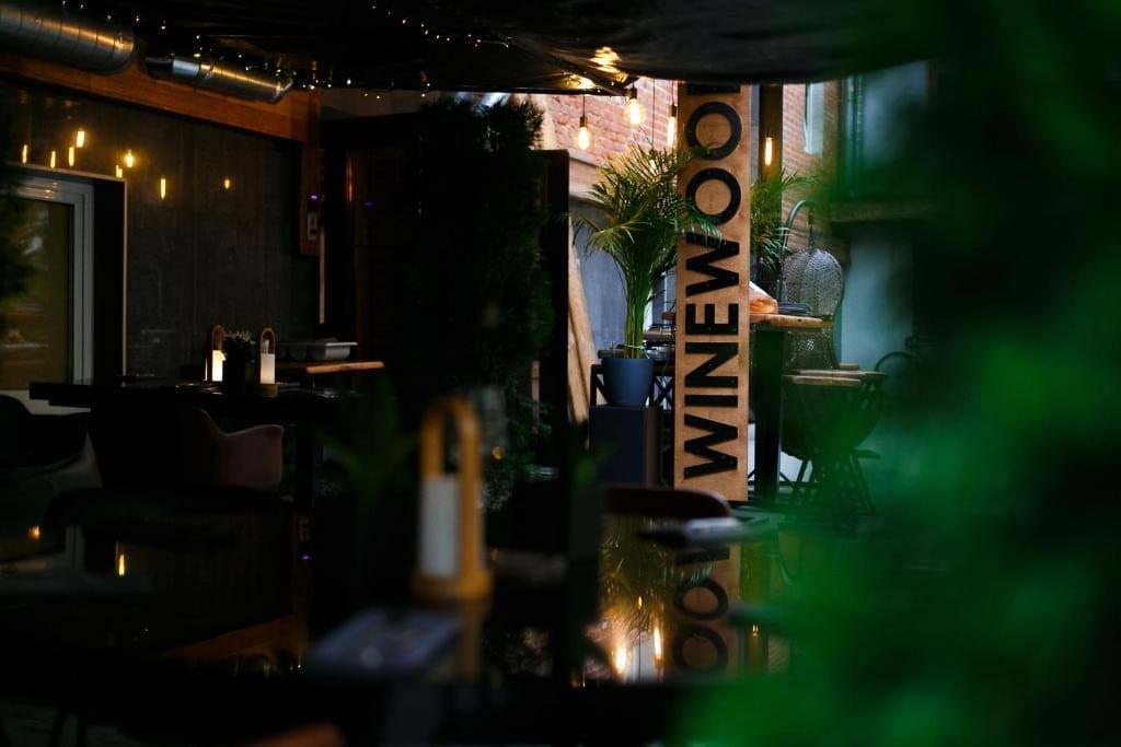 WineWood Garden at night with greenery, tables and the vertical WineWood sign